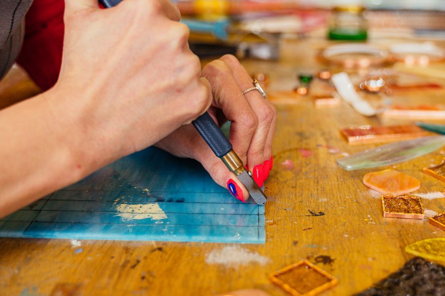 Hands working with stained glass pieces and copper foil at a workbench